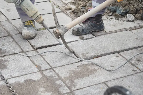 Bir inşaat işçisi geniş fayanslı kaldırımda ustalıkla matkap kullanıyor.