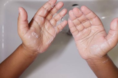 Çocuk, ellerinde sabun ve suyla arındırıcı bir jest yapıyor..