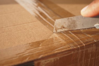 Karton kutuyu dikkatlice açmak için bıçağı ustalıkla kullanan bir elin yakın plan görüntüsü.