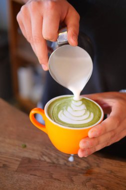 Bir barista ustaca bir matcha latte içine süt dökerek, güzel bir tasarım yaratır..