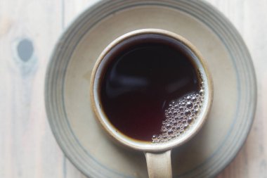 Buharlı ve yeni demlenmiş, köpüklerle süslenmiş bir fincan kahvenin üst görüntüsü.