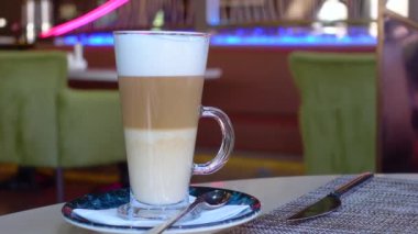 Bir kafede, berrak, uzun bir bardakta servis edilen güzel katmanlı bir latte.