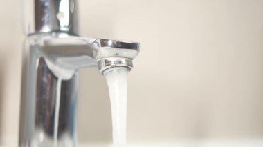 Temiz su zarif, parlak krom bir musluktan akıyor rahat bir mutfak ortamında.