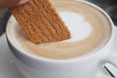 A delightful biscuit is being dipped slowly into a creamy coffee drink featuring beautiful foam art clipart