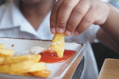 Genç bir çocuk çıtır çıtır, lezzetli bir patates kızartmasının tadını çıkarıyor. Lezzetli bir ketçapa batırılmış.