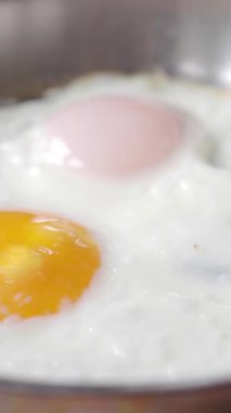 İki kırık yumurta tavada cızırdıyor, canlı bir yumurta sarısı ve narin, yumuşak beyaz