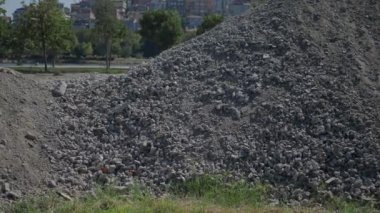 Yoğun bir inşaat alanında, açık mavi gökyüzünün altında büyük bir çakıl ve taş yığını yatıyor.
