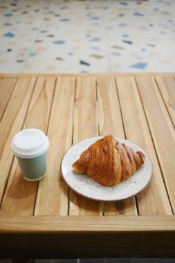 Nefis, taze pişmiş kruvasan, ahşap bir masada, dumanı tüten bir fincan kahvenin yanına yerleştirilmiş.
