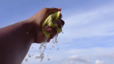 Yavaş çekimde eller mavi gökyüzüne ıslak havlu sıkıyor. 