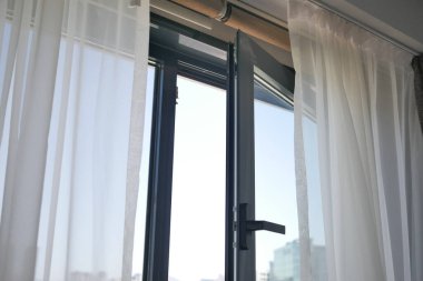 Saf perdelerle örtülmüş neşeli bir pencere doğal ışığı davet eder ve rahat bir atmosfer yaratır.