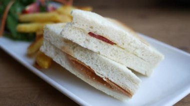 Kızarmış patatesli lezzetli bir sandviç ve beyaz tabakta servis edilen taze bir salata.