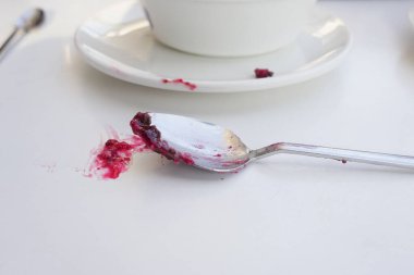 Temiz beyaz bir masanın üzerinde böğürtlen reçeli kalıntısı olan kaşığın detaylı bir yakın çekimi.