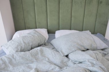 Yapılmamış, dağınık bir yatak, yeşil bir yatak başlığıyla çelişen güzel çiçekli bir yatak.