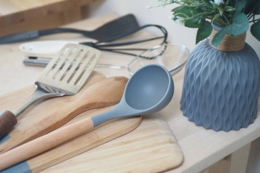 Modern bir mutfakta yemek aletleri ve ahşap bir tezgahta dekoratif bir bitki bulunur.