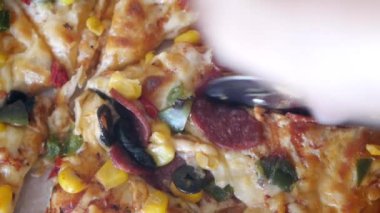 Taze malzemelerle kaplı lezzetli bir pizzayı dilimlemek için pizza kesicisini kullanan bir el..