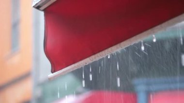 Yoğun, hareketli bir şehir ortamında canlı kırmızı bir tenteden hafif yağmur yağıyor.