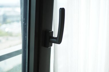 Modern bir pencere kolunun yakından görüntüsü titizlikle hazırlanmış ve perdelere karşı yerleştirilmiş.