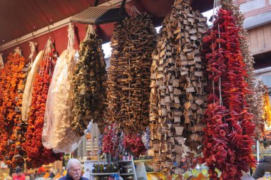Hareketli bir pazarda, canlı bir kurutulmuş biber ve baharat dizisi asılıyor, yoldan geçenleri cezbediyor.