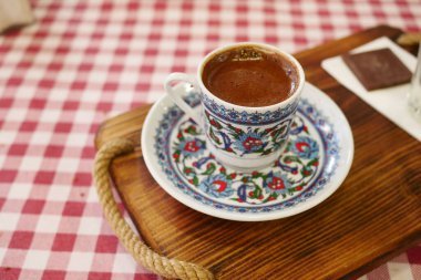 Geleneksel bir çiçekli fincanda servis edilen dumanı tüten Türk kahvesi kareli bir masa örtüsü. Kültürel, aşçılık ve ev temalı projeler için mükemmel..