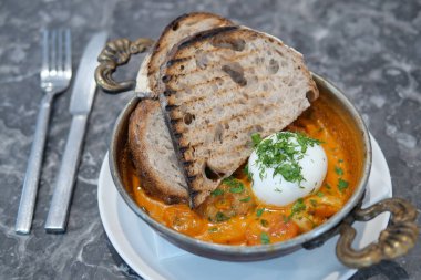 Lezzetli bir shakshuka, haşlanmış yumurta ve çıtır ekmekle lezzetli bir şekilde servis edilir.