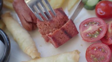 Bir tabak ızgara sosis, kızarmış patates ve taze sebze, hepsi lezzetli ve lezzetli.