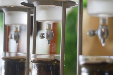 Kafe ortamında kahve demleme aparatının yakın çekimi, soğuk kahve yapımında kullanılan süreç ve ekipmanları gözler önüne seriyor. Görüntü modern ve profesyonel kafe atmosferini vurguluyor..,