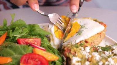 Üzerinde kızarmış yumurta ve taze salatayla avokado tostu olan canlı bir tabak..