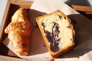 Sıcak bir kruvasan ve tahta tepside sanatsal olarak servis edilen bir parça mermer kek.