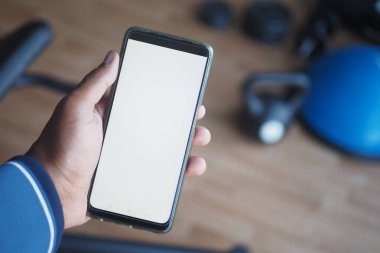 Jimnastik salonunda elinde akıllı bir telefon tutan ileri düzey fitness teknolojisi sergileyen biri.