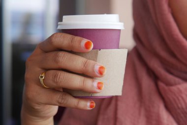 Bir el zarif bir şekilde kırmızı turuncu tırnaklı bir kahve fincanı tutuyor, günlük geziler için ideal.