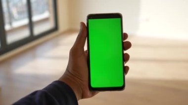 Bir insan, canlı yeşil bir ekran gösteren modern bir akıllı telefon tutuyor.