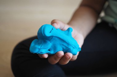 Bir çocuk gururla renkli mavi bir kil modelleme figürü tutar, yaratıcılığını gösterir.