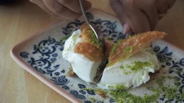 Ağız sulandıran bir baklava tatlısının yakın plan görüntüsü kremalı süslemeli ve zarif bir çiçek tabağında taze şam fıstığı serpiştirilmiş. Geleneksel tatlıları sergilemek için mükemmel.