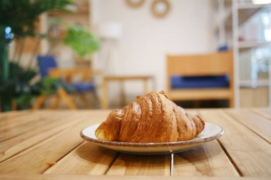 Taze pişmiş, lezzetli bir kruvasan kırsal bir ahşap masada zarif bir şekilde oturur.