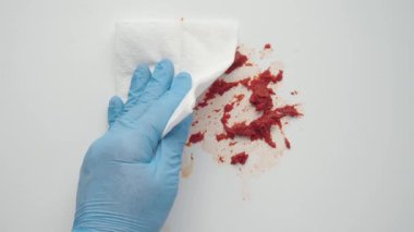Eldivenli bir el, kağıt havlu kullanarak yüzeydeki kırmızı lekeyi temizler.