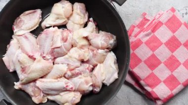 Taze çiğ tavuk kanatları tavada lezzetli bir şekilde cızırdıyor, kareli bir kumaşın yanında.