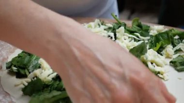 Yaşlı bir el nazikçe hamurun üzerine bol miktarda peynir serper.