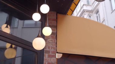 Zarif asılı ışıklar ve sıcak bir tente içeren şık bir kafe girişi.