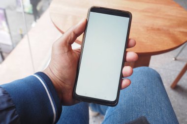 Bir el, rahat bir kafede otururken boş bir ekranla şık bir akıllı telefonu tutar.