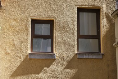 İki zarif pencere yıpranmış bir duvara benzersiz gölgeler bırakıyor ve ilginç bir etki yaratıyor.