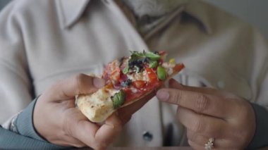 Bireyin elinde çeşitli taze malzemelerle kaplı bir pizza dilimi var.