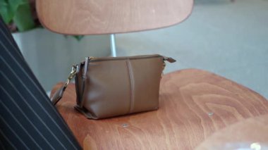 Şık kahverengi deri bir çanta bir sandalyeye gelişigüzel yerleştirilir ve estetik dekora eklenir.