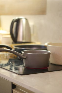 Şık ve modern bir mutfak, çeşitli tencereler ve sobanın üzerine zarif bir çaydanlık sergileniyor.