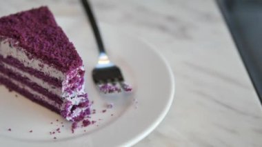 Zarif bir mermer masa üzerinde yumuşak bir kremayla kaplı mor katmanlı bir pasta dilimi.
