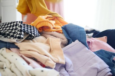 Çeşitli giysiler bir yatağa saçılmış, canlı ve renkli bir çamaşır sahnesi yaratıyor.