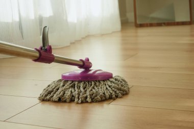 Canlı ve renkli bir paspas güzel bir güneşli odada ahşap bir zemini etkin bir şekilde temizliyor.