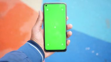 Bir insan, doğadayken canlı yeşil bir ekran gösteren akıllı bir telefon tutuyor.