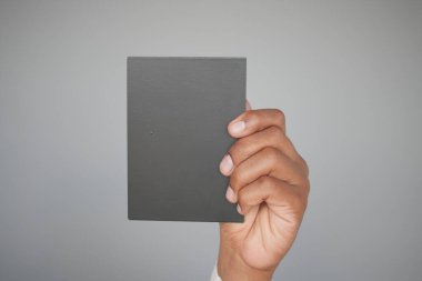 Arkasında yumuşak gri bir zemin olan boş siyah bir kitabı nazikçe tutan bir el.