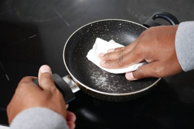 Bir insan, tavayı kağıt havluyla titizlikle temizlerken fırının üstüne yerleştirir.