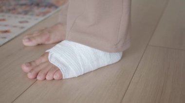 Ahşap zemine sarılı tıbbi bandajla insan ayağının yakın görüntüsü.